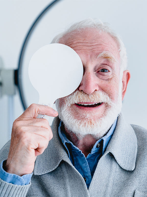older man reading a vision test with one eye covered at the eye doctor